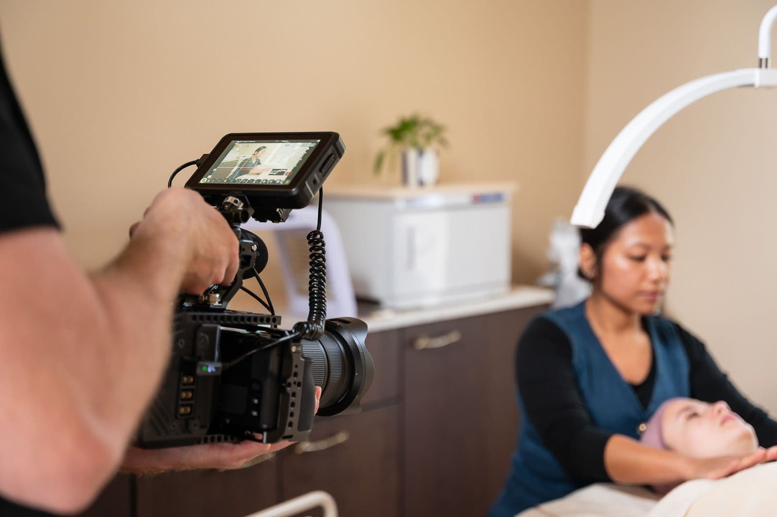 Camera rolling in a salon, a practitioner at work on her client in the background