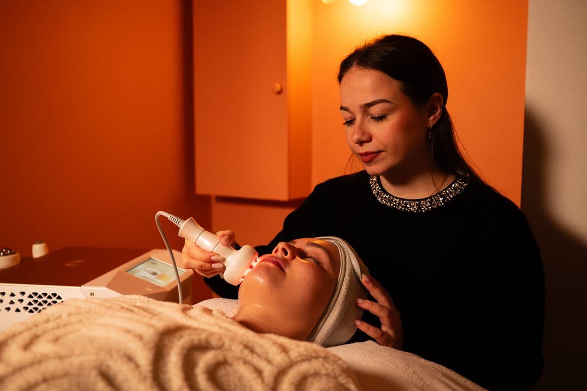 Cabine de spa en lumière tamisée, praticienne réalisant un soin du visage sur une cliente enveloppée d'un plaid