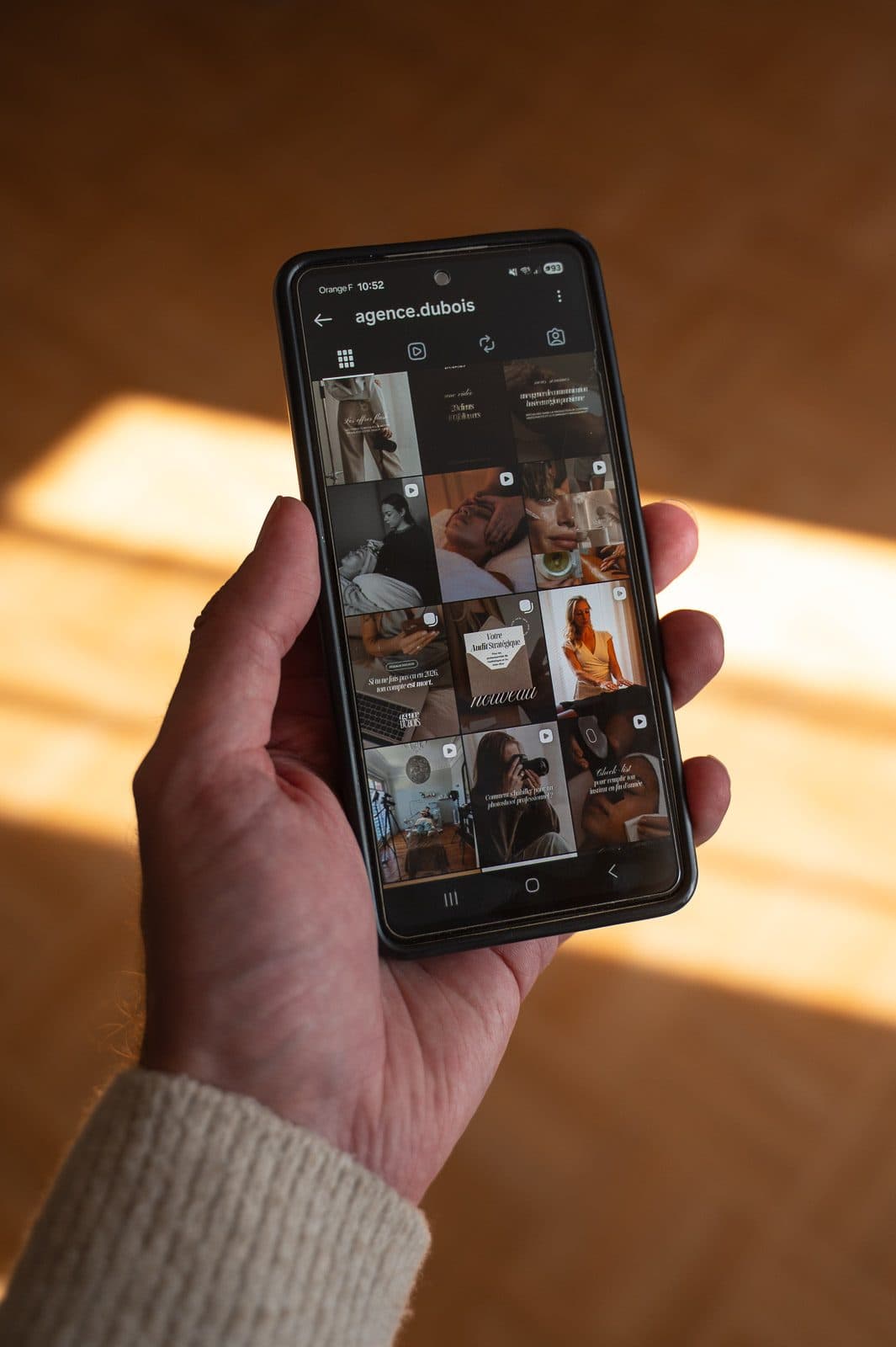 Hand holding a smartphone showing a spa's Instagram feed, in low golden light