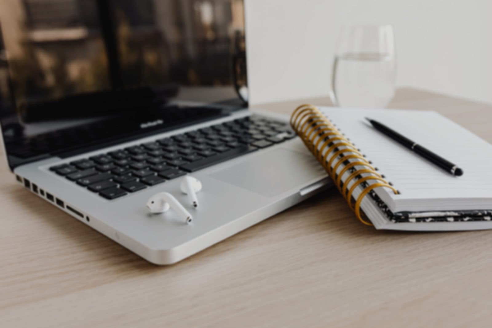 Open laptop beside a spiral notebook and a pen, on a light desk