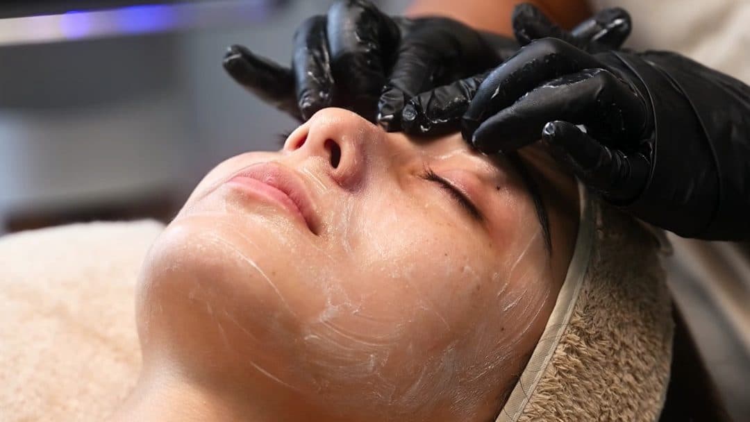 Facial treatment in a salon, gloved hands applying a product to a reclining client
